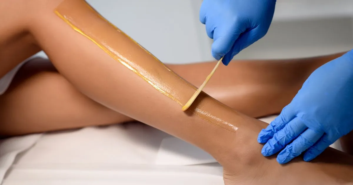 Esthetician performing leg waxing treatment on a client in Minot, ND